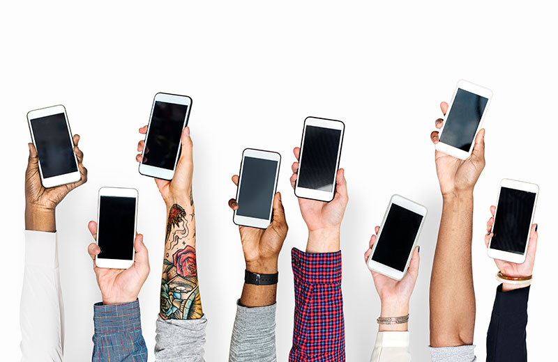 8 different people's hands holding smart phones up in the air